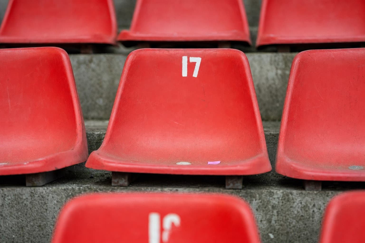 Empty red plastic seat in a worn football stadium tier, overcast natural light.